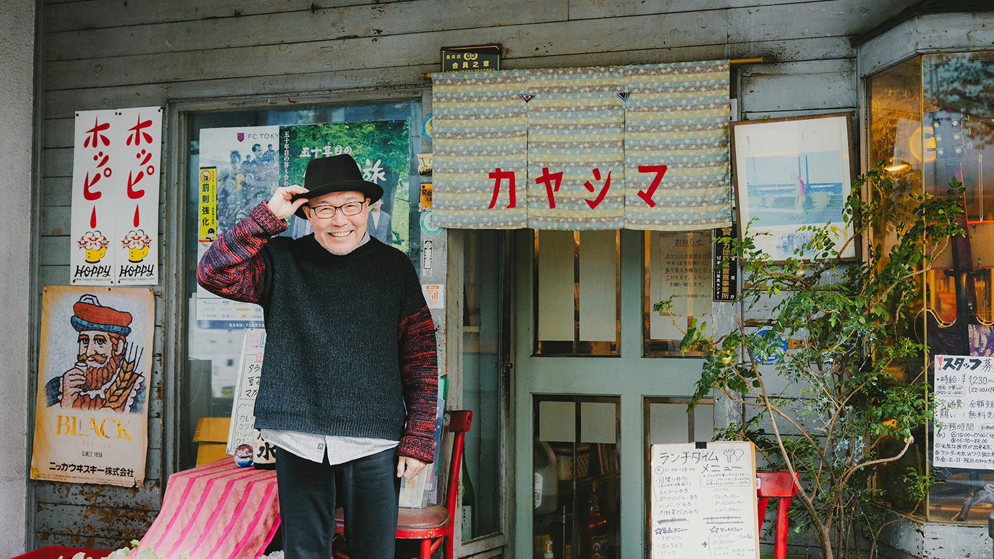 喫茶店「カヤシマ」の入口前で、帽子に手を添えて笑顔で立つ久住昌之さん
