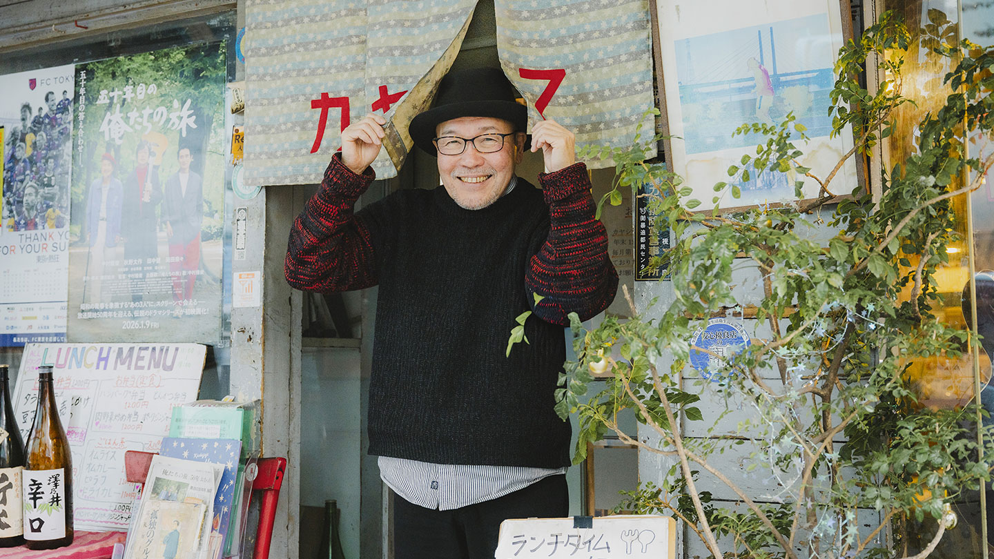 喫茶店「カヤシマ」の入口で暖簾を持ち上げ、笑顔を見せる久住昌之さん