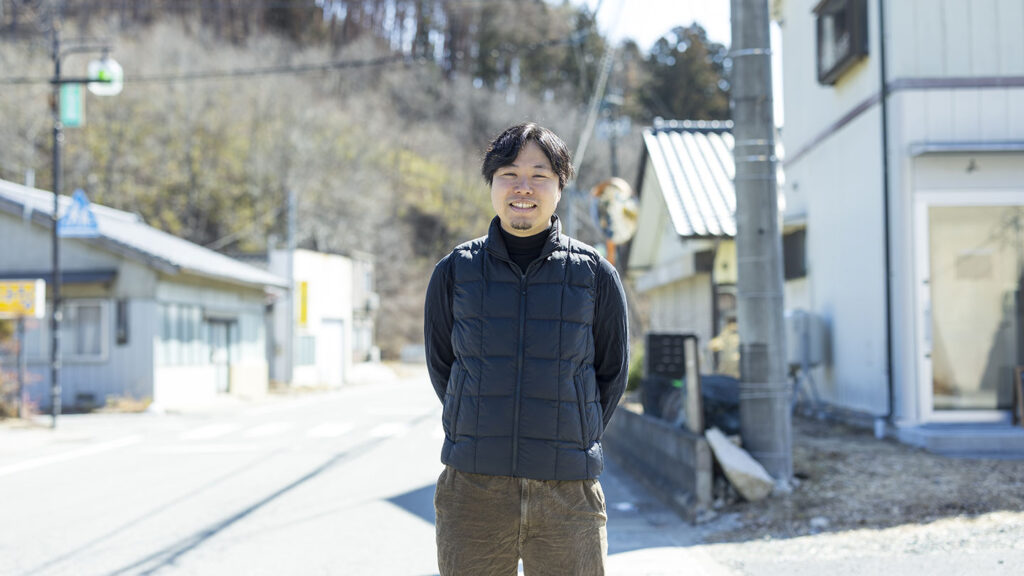川内村の山を背景に微笑む、株式会社Kokage 代表取締役 /「naturadistill 川内村蒸溜所」代表の大島草太さん