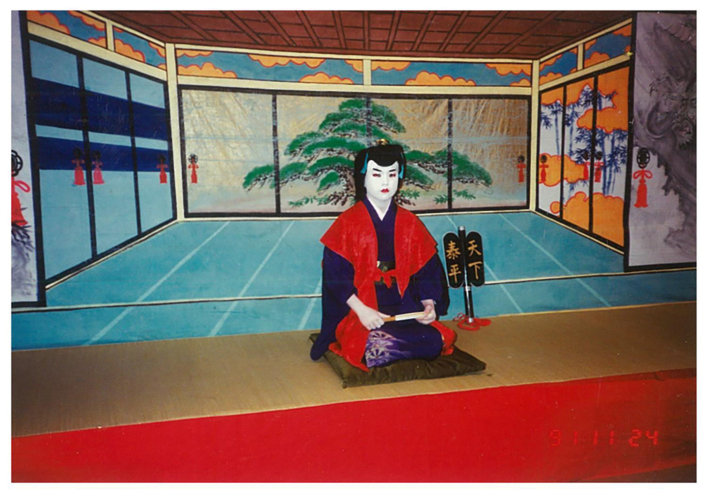 農村歌舞伎の舞台で、化粧と衣装をまとった少年時代の青山草太さんが座っている様子