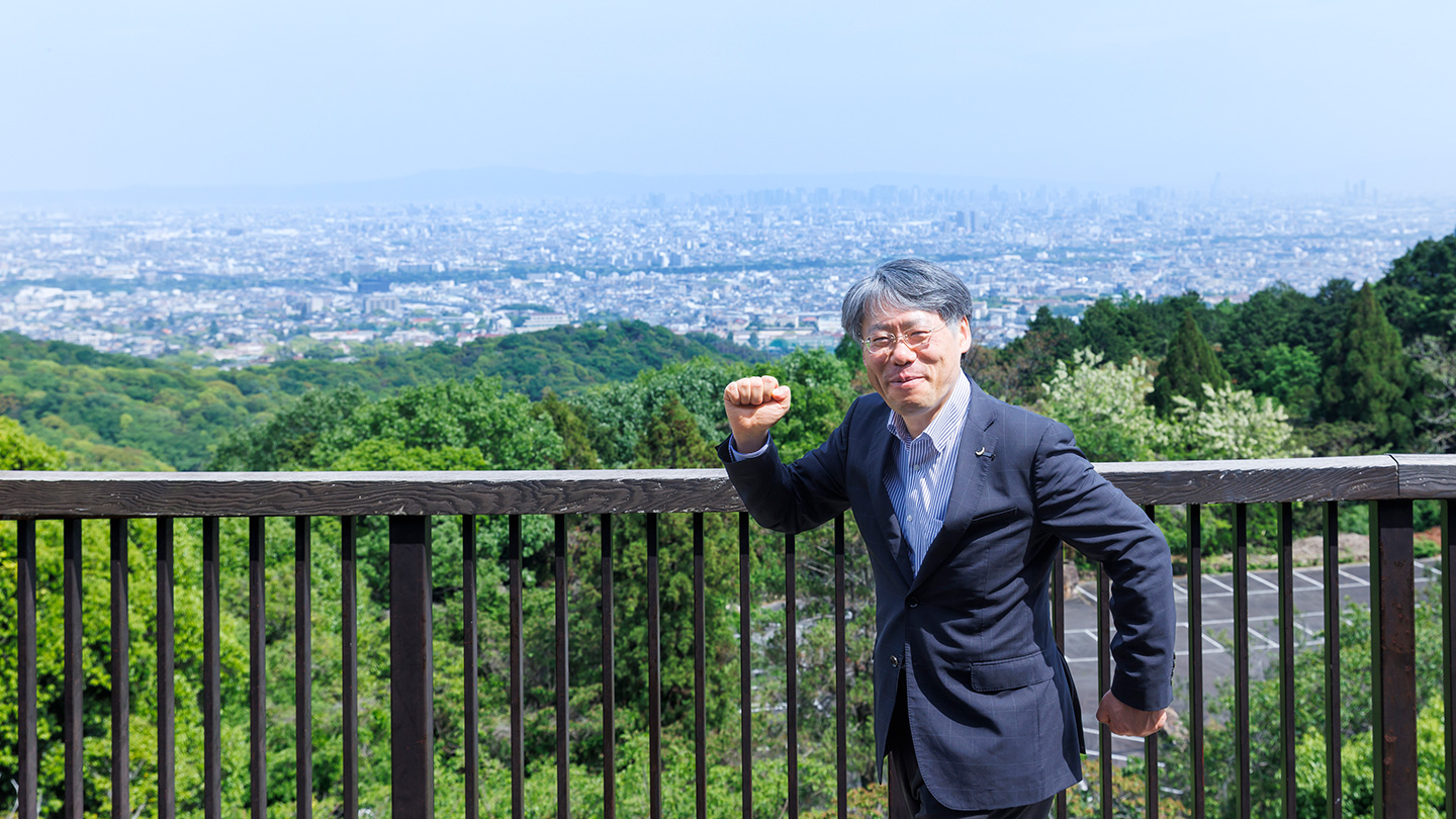 展望台からの景色を背景に「出発」のポーズをとる島村さん