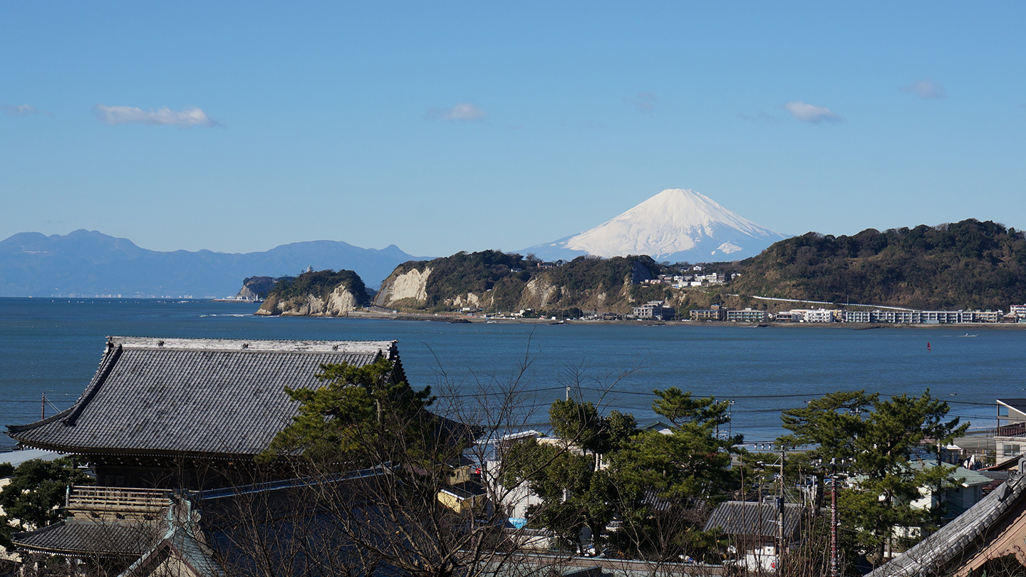 寺院の背景に広がる海と、奥に雪が積もった富士山が見える
