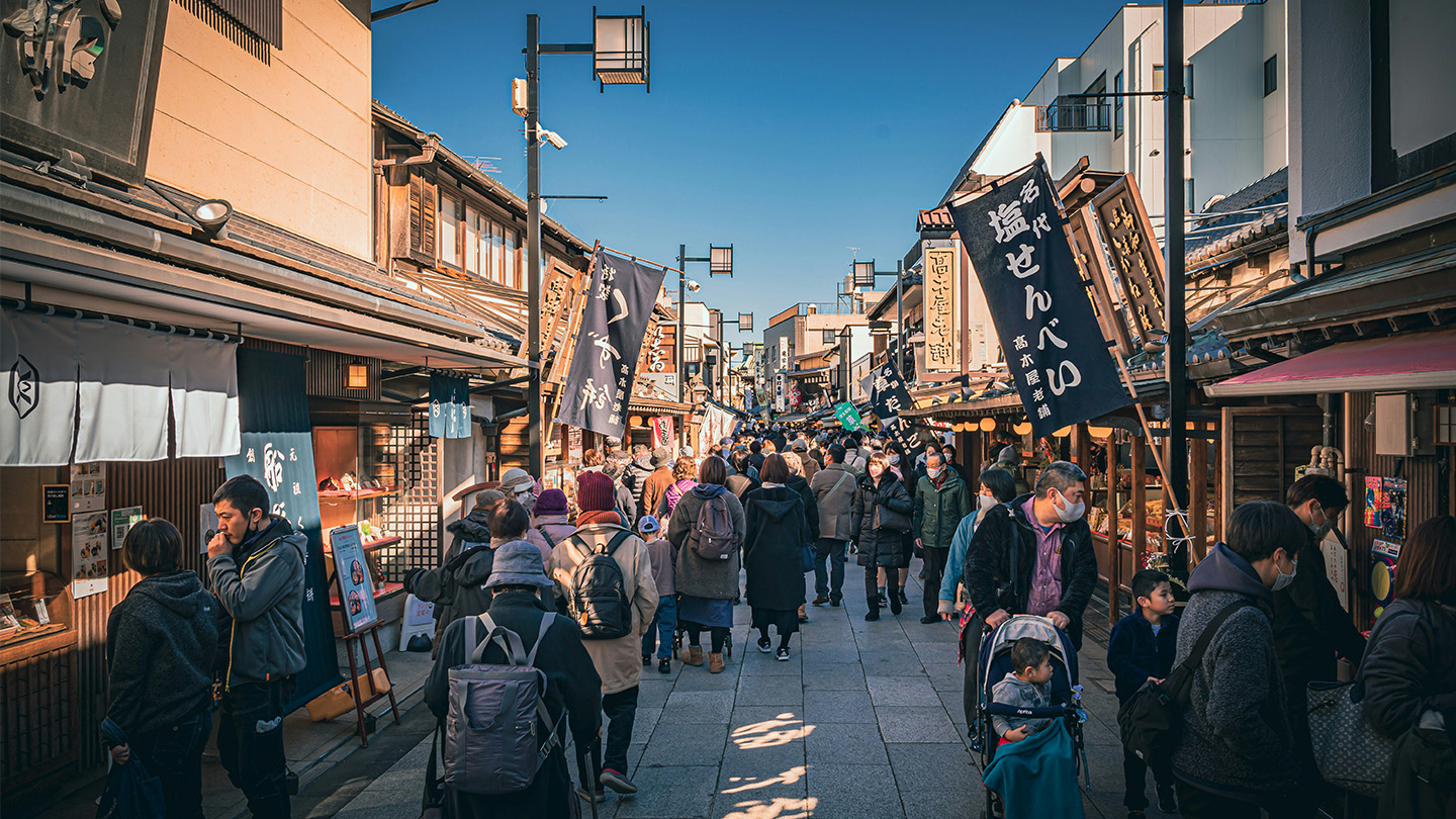 和風の建物が並ぶ商店街を、多くの観光客や買物客が行き交っている
