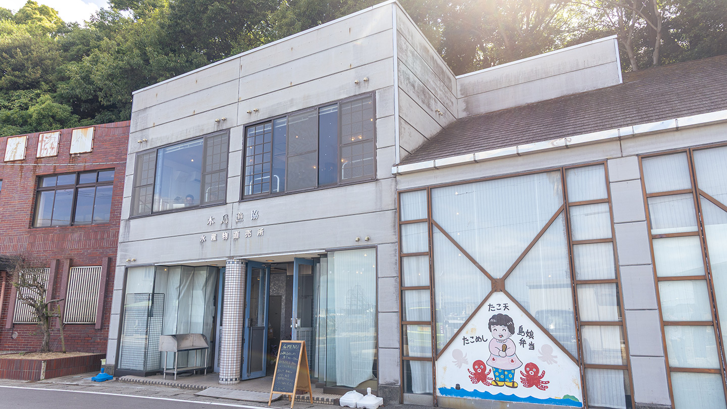 通り沿いに立つライトグレーの外壁の建物。右側のシャッターには、女性とタコのイラストが描かれている