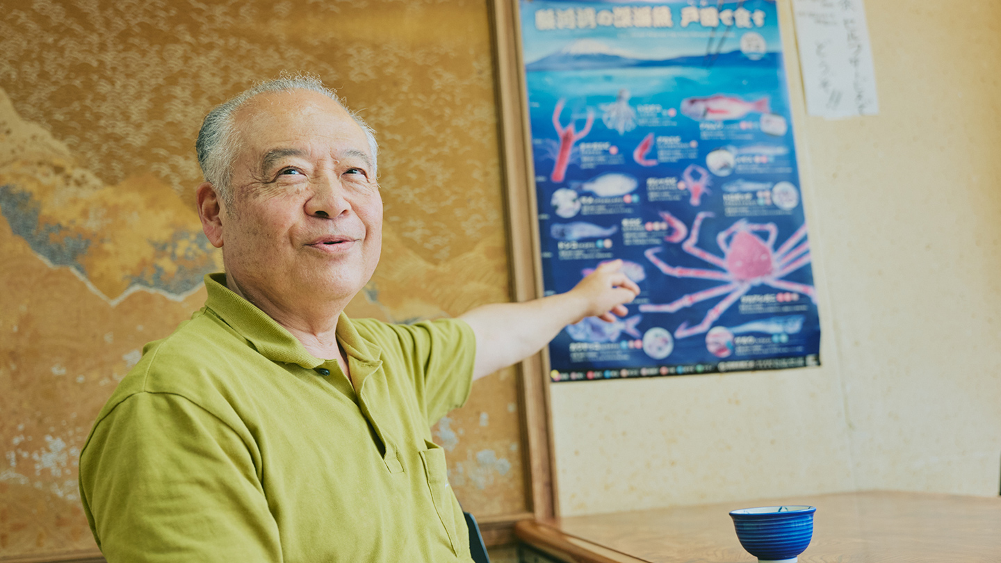 深海魚を紹介するイラストポスターを指さし、笑顔を浮かべる中島さん