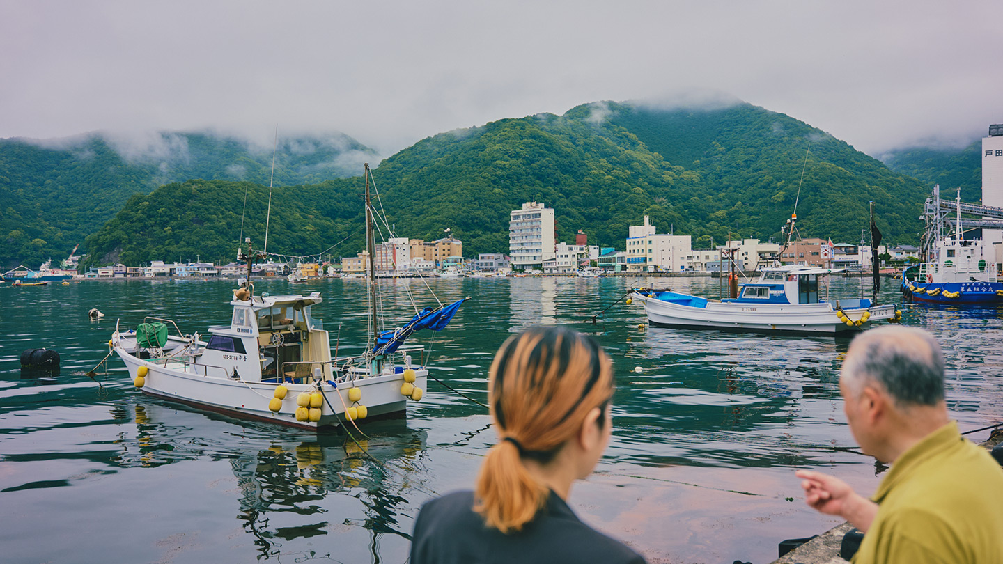 漁港を背景に話をしている中島さんと青山さん