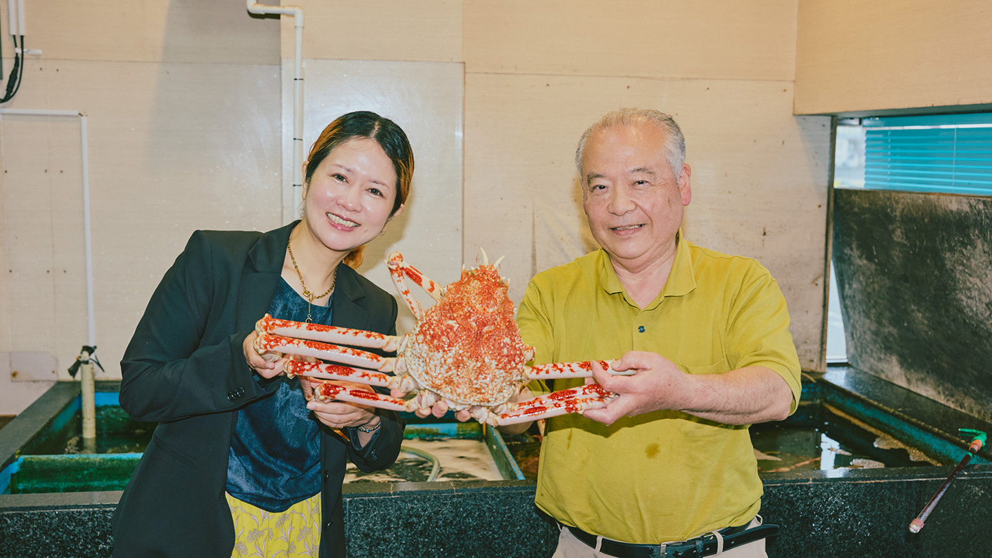 1杯のタカアシガニを二人がかりで持つ中島さんと青山さん。背景には生け簀がある