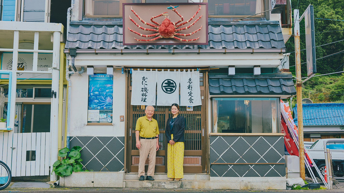 かに・磯料理」と書かれた店の暖簾の前に立つ中島さんと青山さん