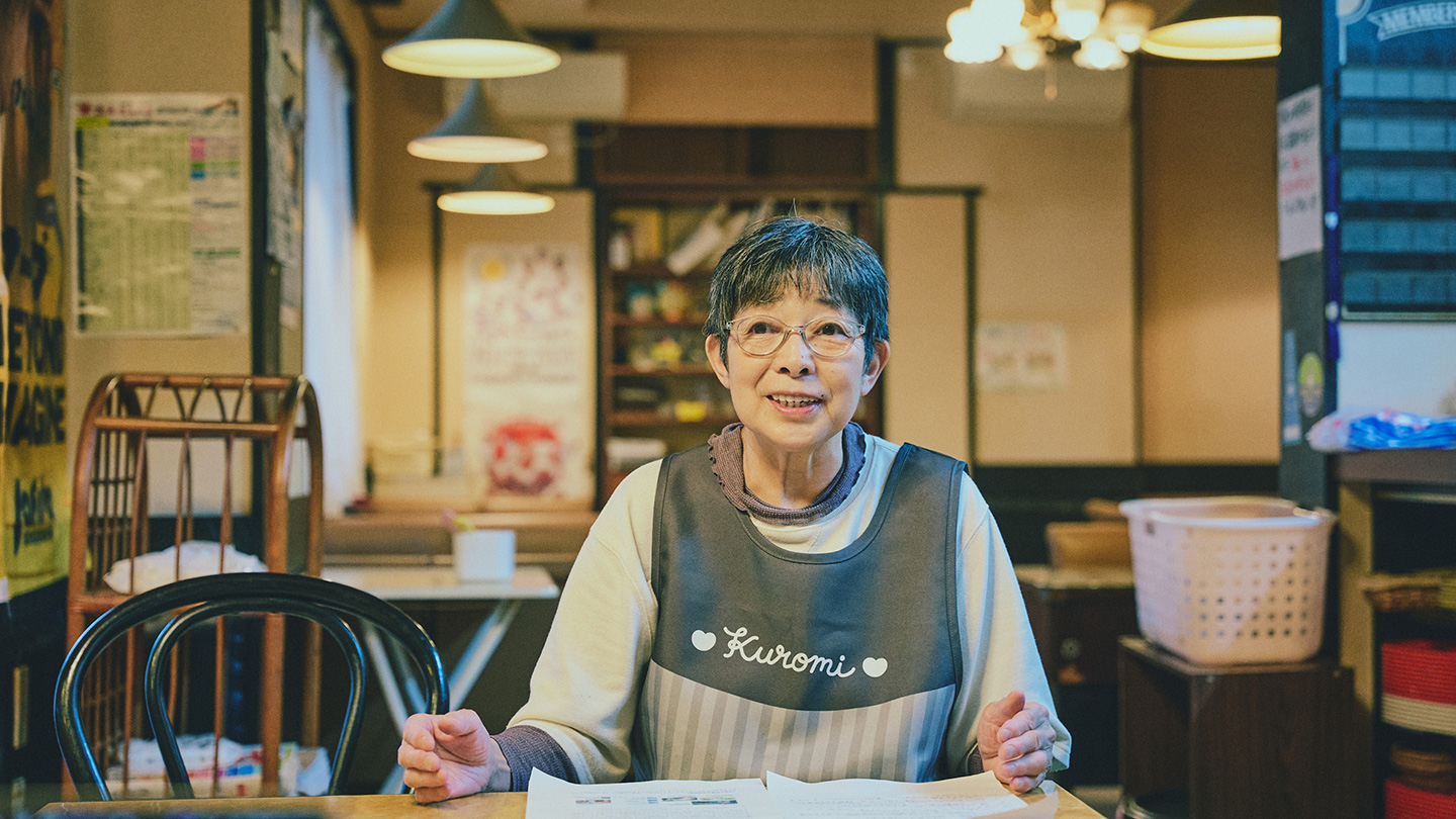 飲食店の店内で、エプロン姿でインタビューに答える大野マサ子さん