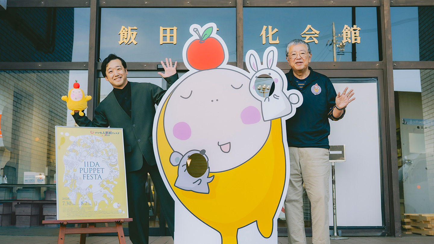 いいだ人形劇フェスタの公式キャラクター「ぽぉ」の顔ハメパネルを挟んで立つ後藤さんと原田さん