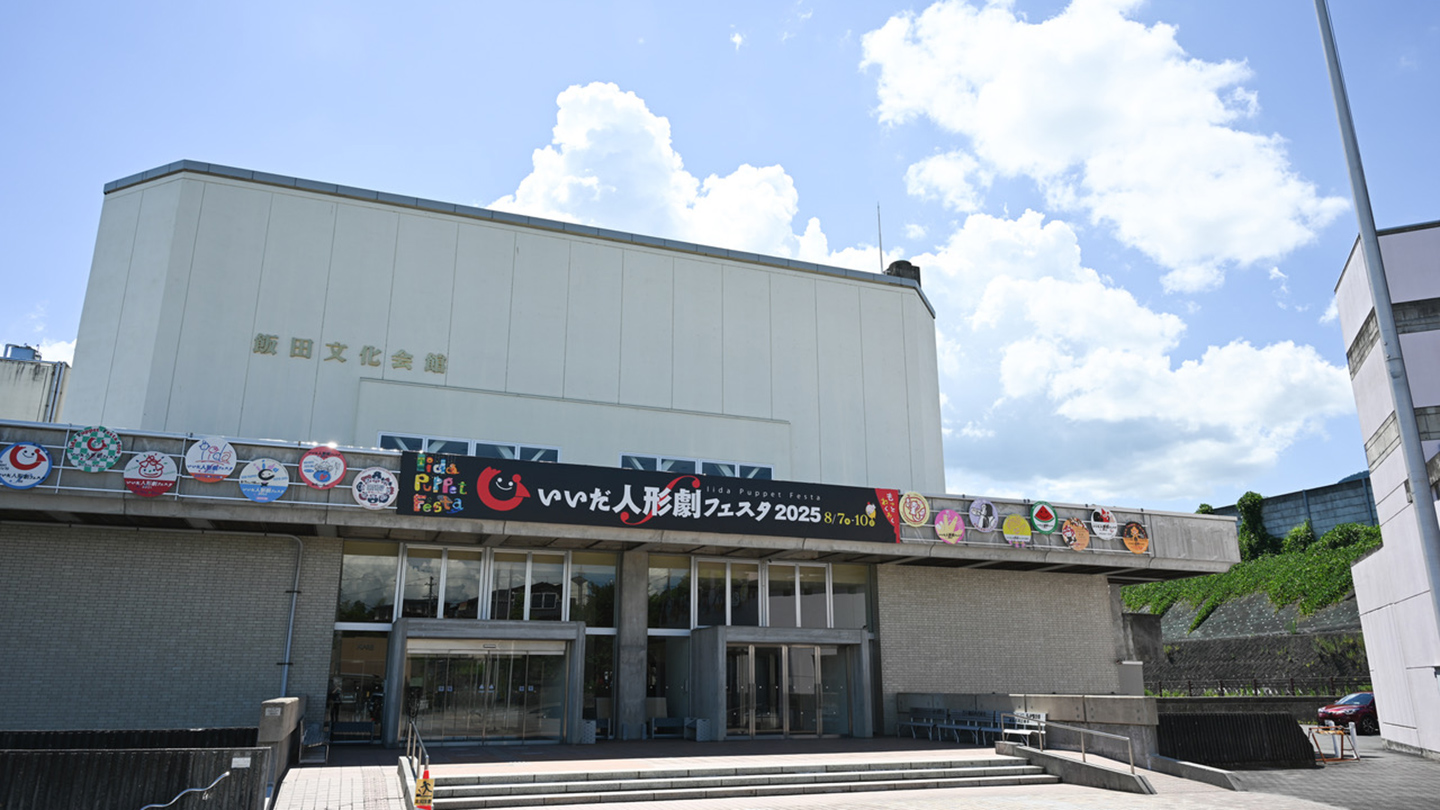 「いいだ人形劇フェスタ2016」と書かれた看板と、歴代ワッペンを模した看板が飯田文化会館に掲げられている