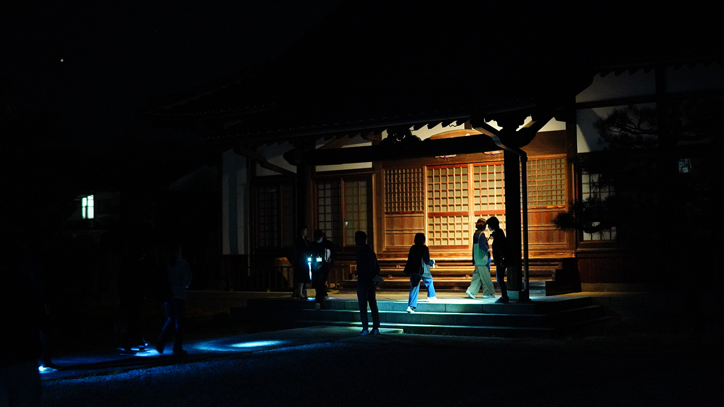 懐中電灯に照らされた夜道を進むゴーストツアー参加者