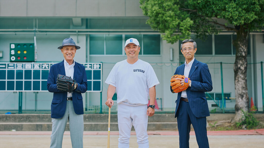 野球のグラウンドにグローブやバットを手にした坂口清貴さん、藤井潤作監督、石榑淳さんが立っている