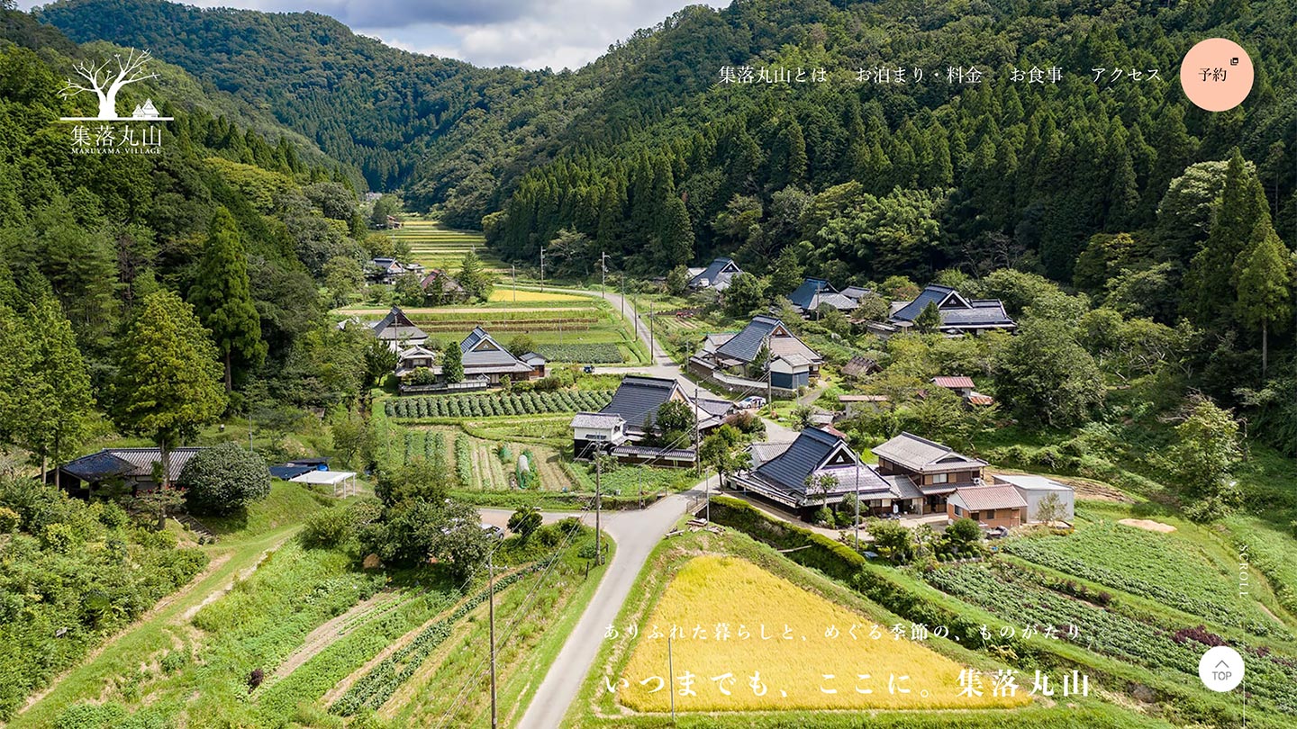 山あいの集落に、田畑や道路、家屋が広がっている様子。周囲には緑豊かな山林が広がっている