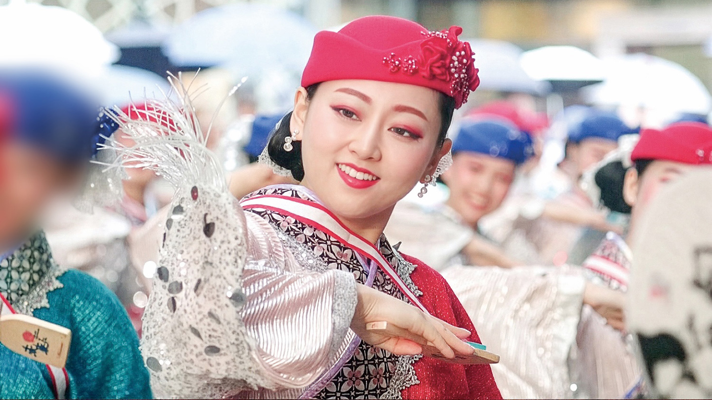 ピンク色の帽子を被り、鳴子を持って踊る山本さん