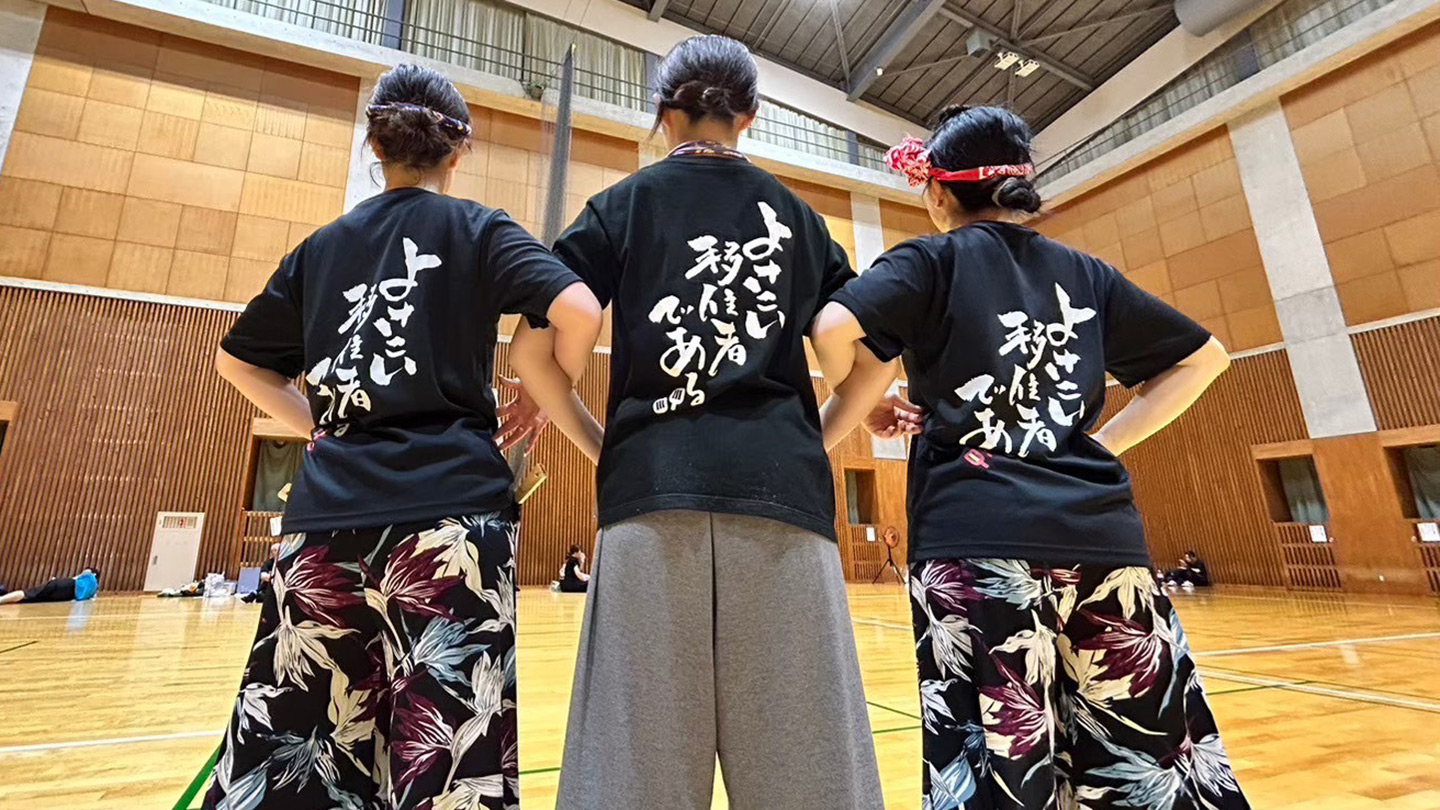 体育館で踊り子たちが後ろを向き、腕を組んで立っている様子