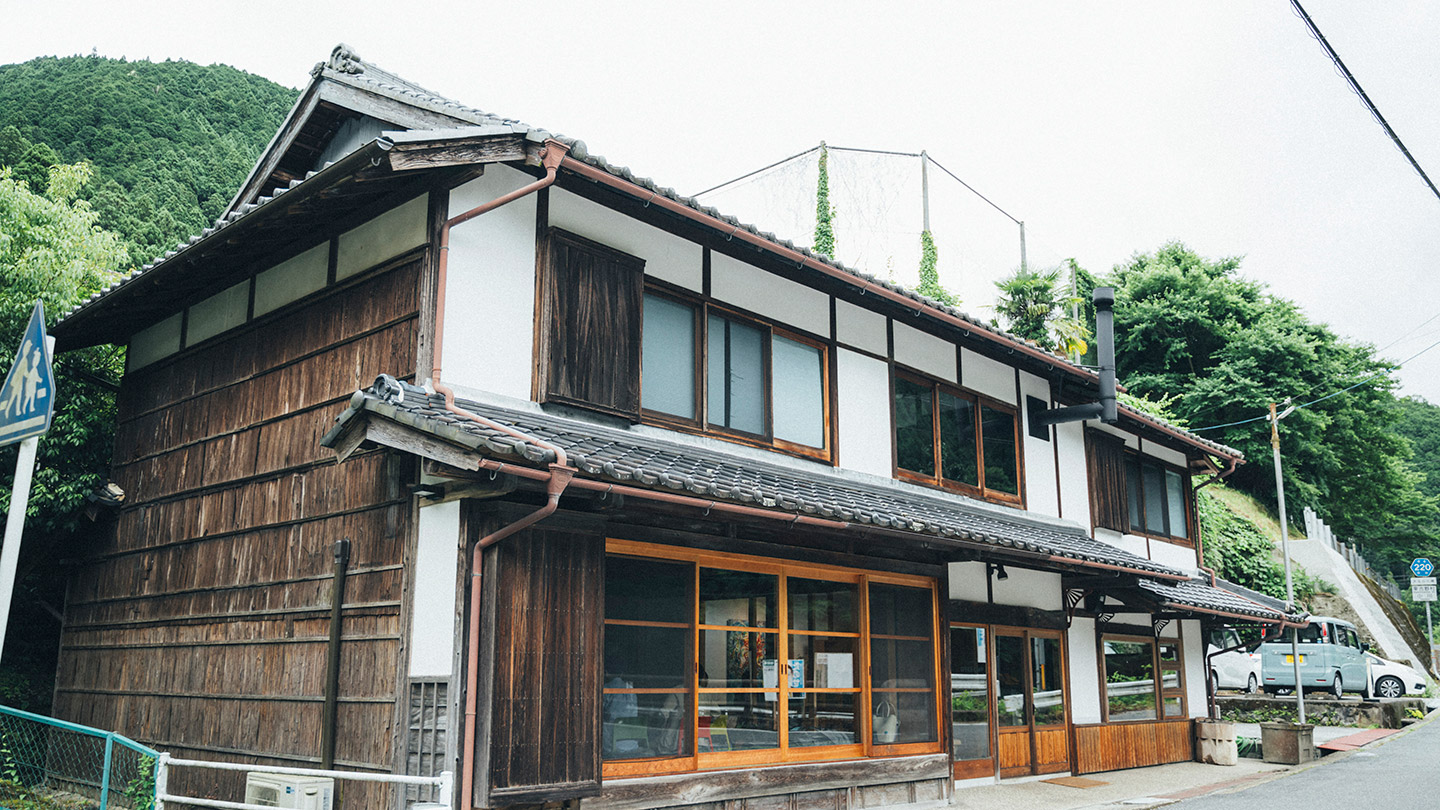 古民家を改修した建物が、緑に囲まれた道路沿いに建っている
