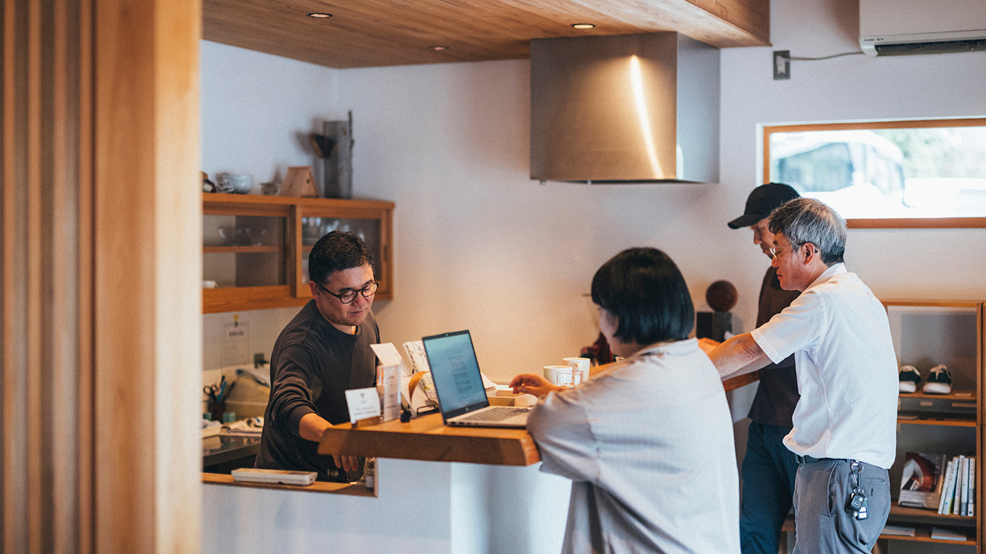 木を基調とした室内で、複数の人物がカウンターを囲んでいる