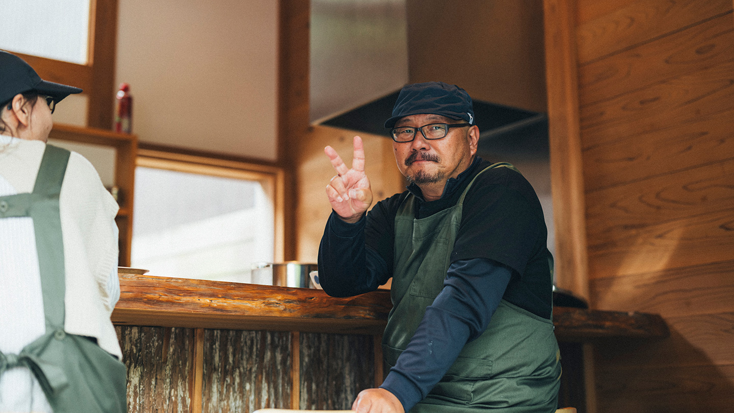 木を基調とした店内で、エプロン姿の人物がピースサインをしている