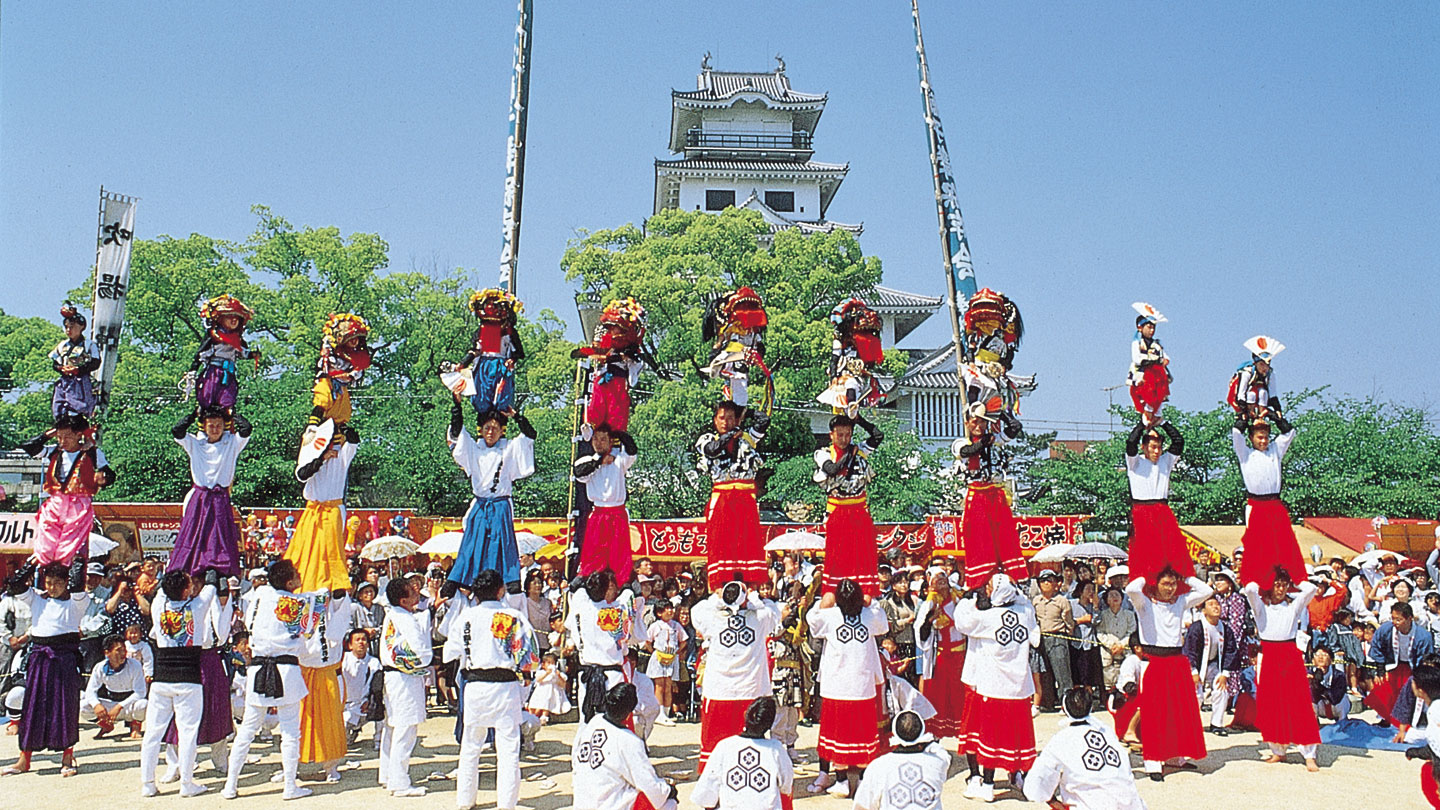 城を背景にした広場で、色鮮やかな衣装を着た人々が伝統芸能を披露している