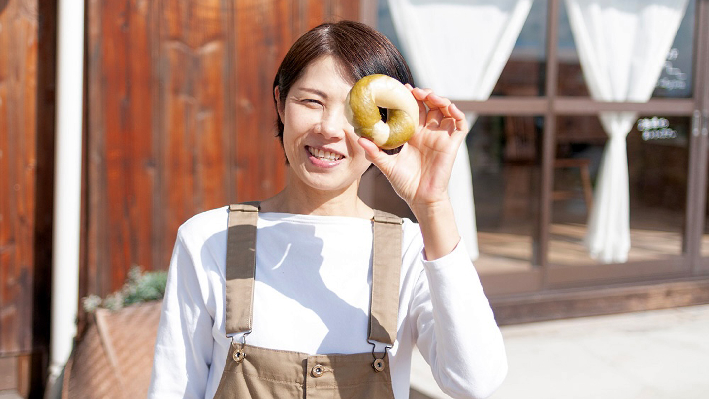 佐々木さんがベーグルを手に笑顔を見せている