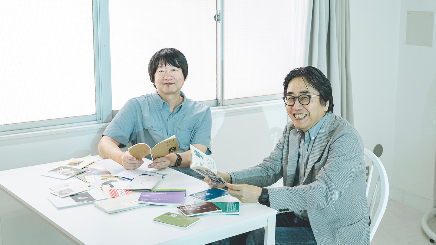 テーブルに並べられたZINEを手に取りながら、仲俣暁生さんと橋本誠さんが笑顔を浮かべている