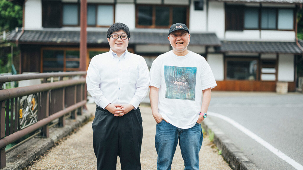 古民家を背景に、北川拓哉さんと坂本大祐さんが笑顔を見せている