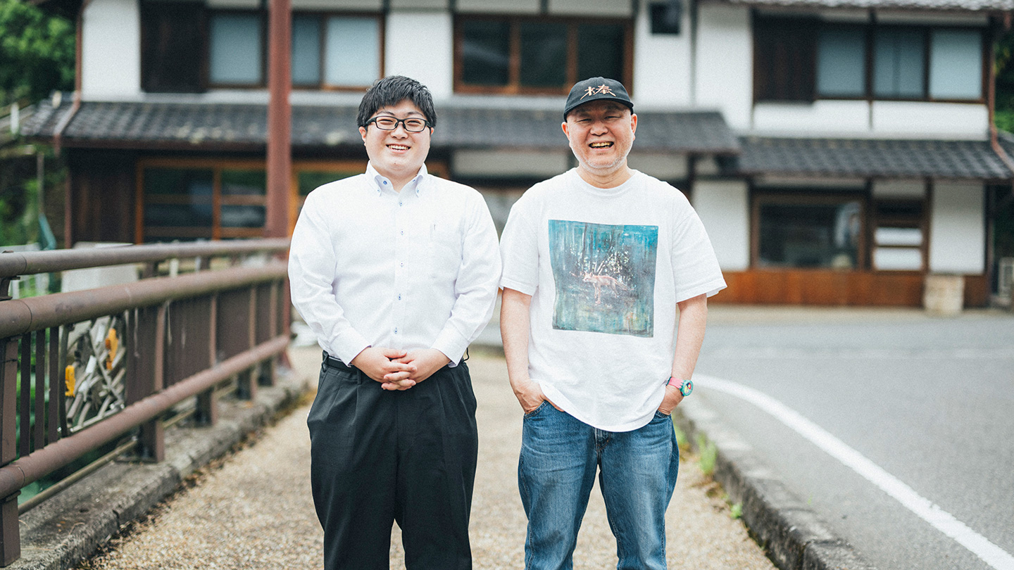 古民家を背景に、北川拓哉さんと坂本大祐さんが笑顔を見せている