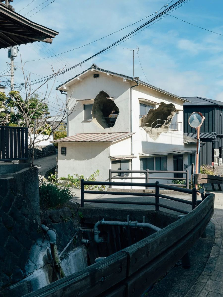 街中の白い壁の民家の壁に、大きな穴が開いている作品