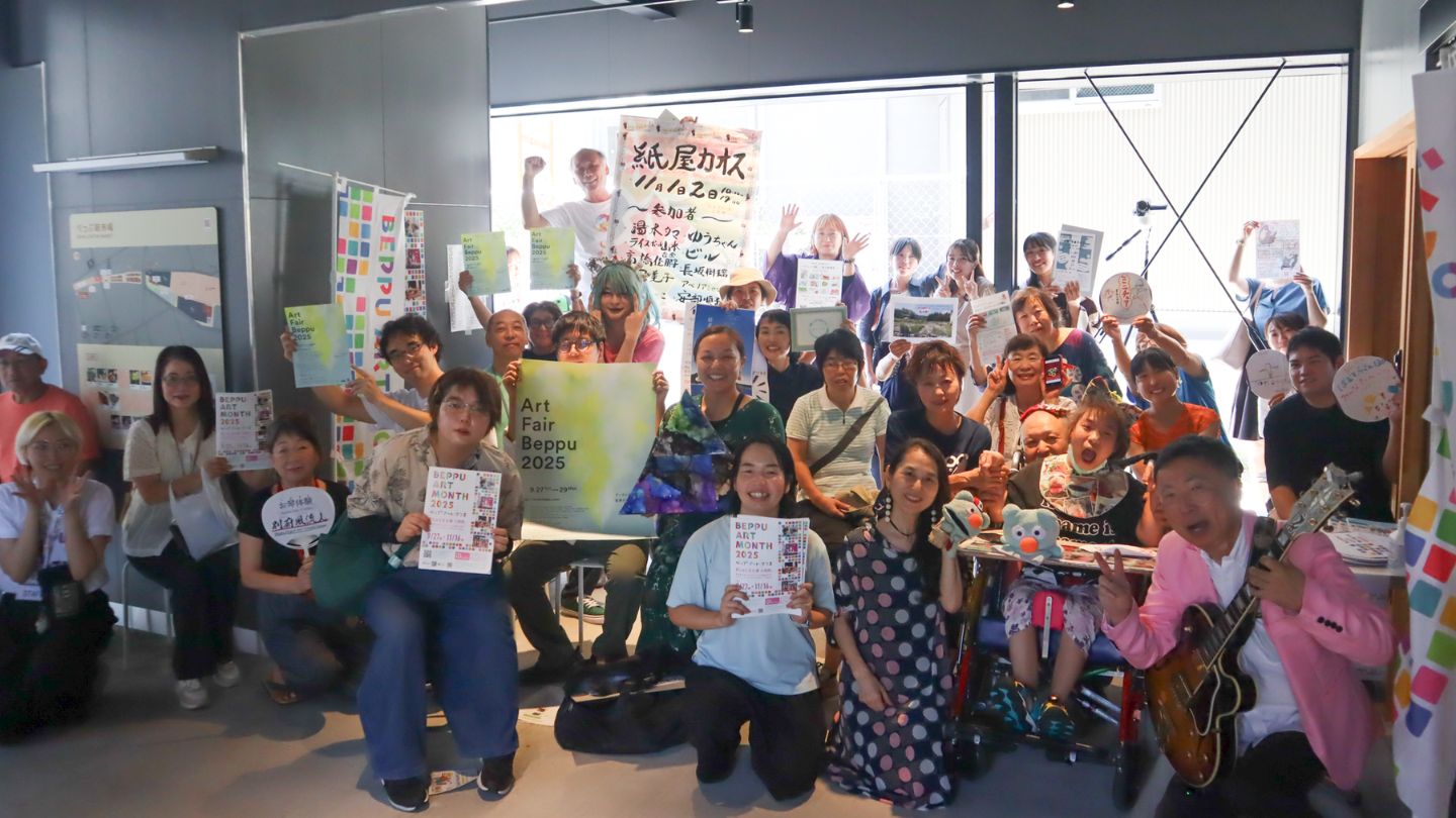 『BEPPU ART MONTH』と書かれたパンフレットを持って30人ほどのイベント参加者が笑っている