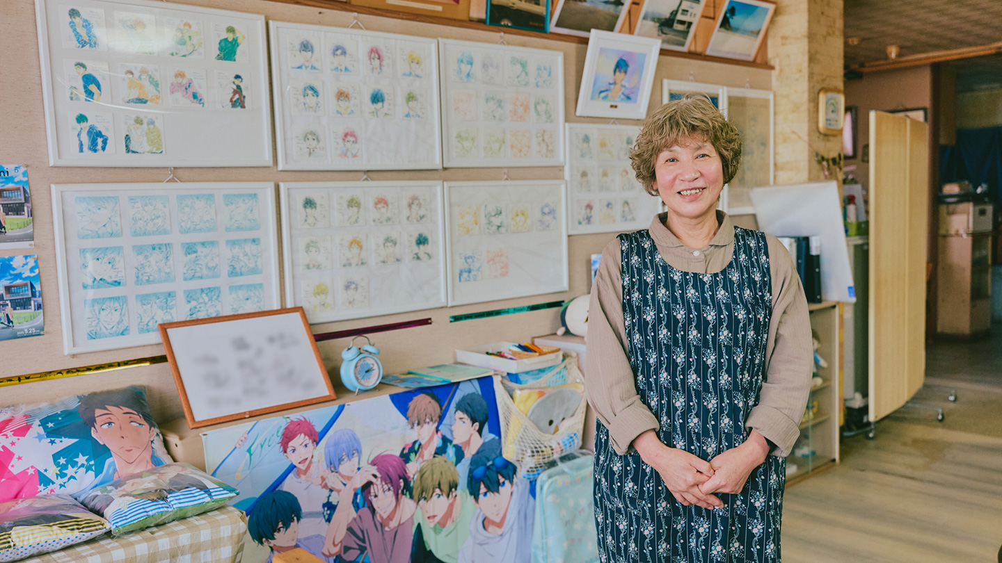 『Free!』のグッズが並ぶ宿のロビーに立つ恵さん