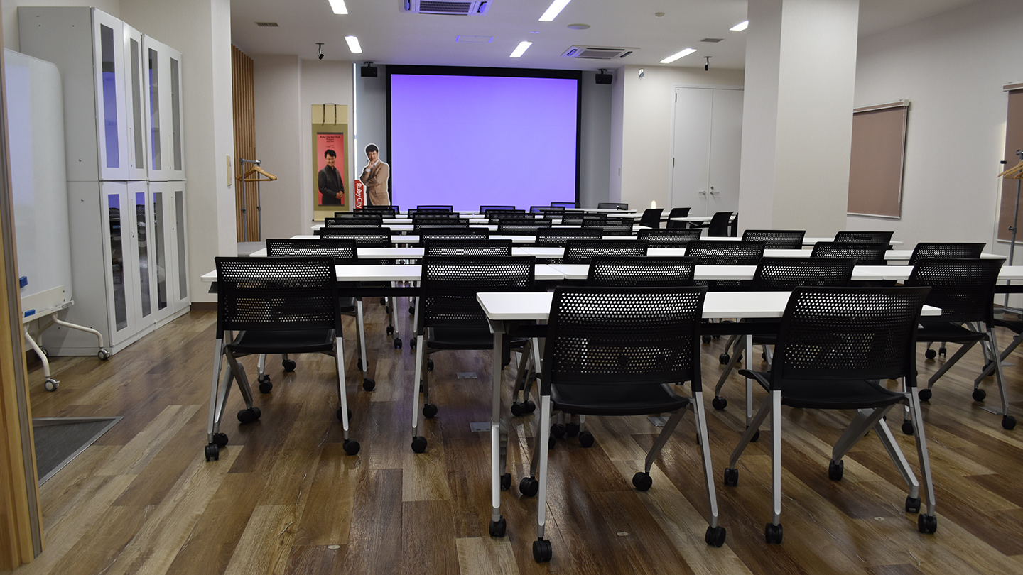 プロジェクターの前に会議用の机とテーブルが並べられている