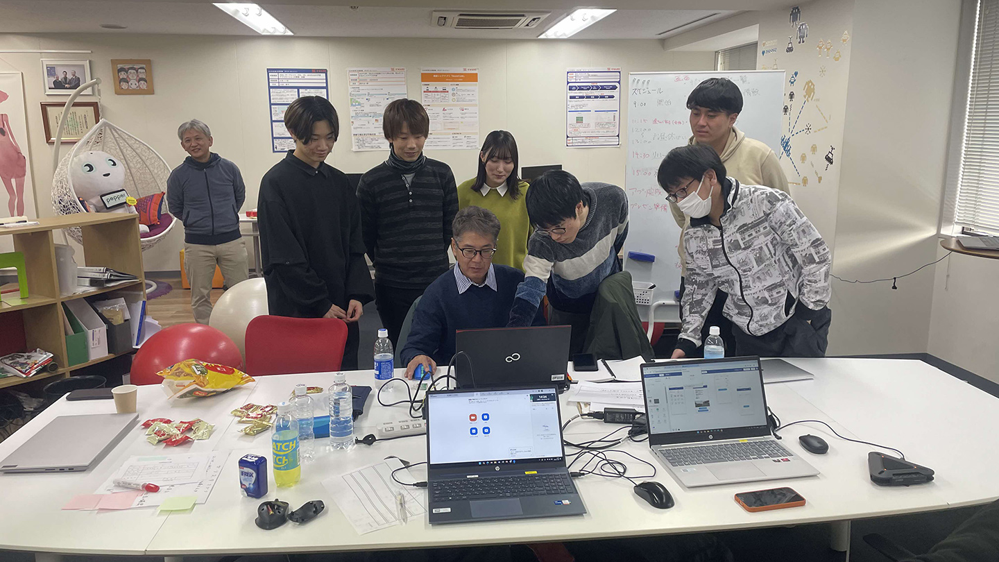 PCに集まって画面を見ながら話し合うエンジニアたち