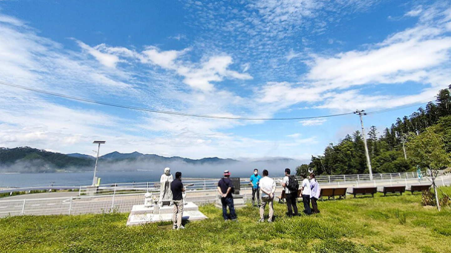 と山を望む芝生広場で、参加者が集まり説明を聞いている
