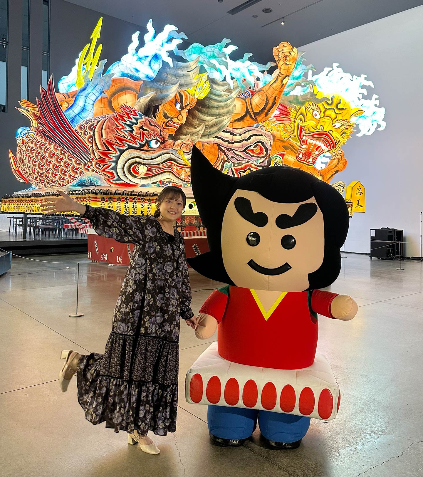 大型のねぶたを背景に、キャラクターと並んでポーズをとる三上さん