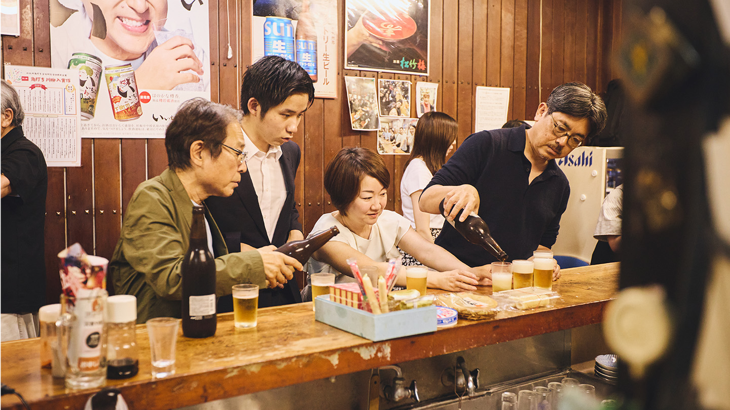 ビールを各々のコップに注ぐ江藤さんと、それを見ている角文研のメンバー
