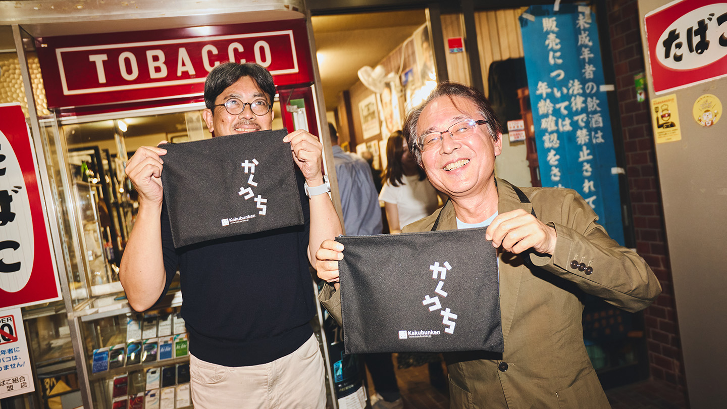 「かくうち」と書かれたサコッシュを掲げる江藤さんと吉田さん